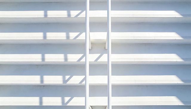 Sunlit Minimal White Staircase Casting Sharp Geometric Shadows with Symmetrical Handrails