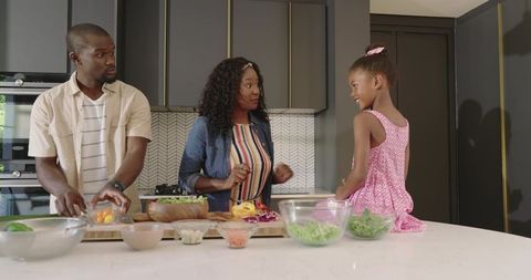 Parents and daughter preparing colorful salad together on modern kitchen island