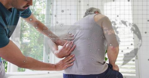 Caregiver helping elderly man with back pain at home, hands-on support and comfort