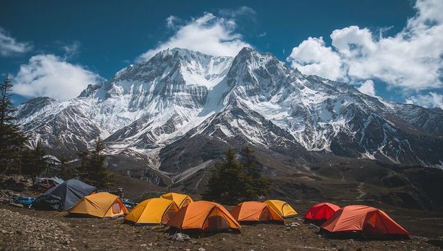 Snowcapped peak overlooking colorful alpine campsites on rocky plateau under dramatic sky