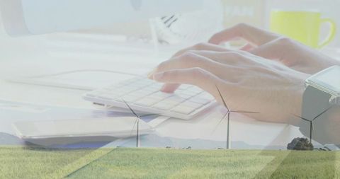 Typing hands overlaying wind turbines creating renewable energy business and tech concept