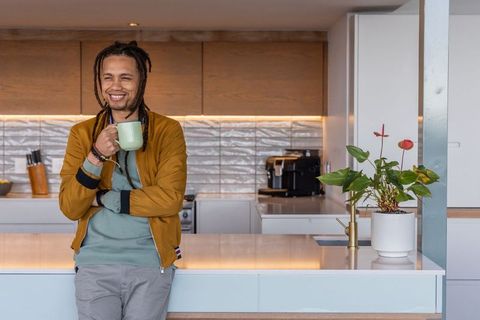 African american man leaning on kitchen island holding coffee mug and smiling