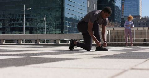 African american runner tying shoe on urban rooftop plaza with woman checking smartphone