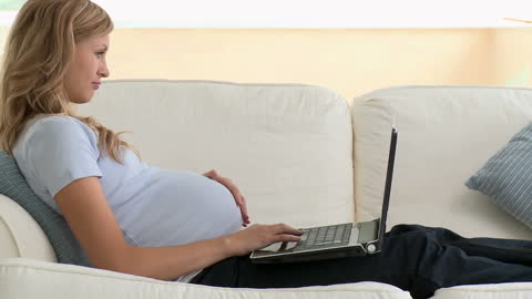 Pregnant Woman Relaxing with Laptop on Sofa at Home