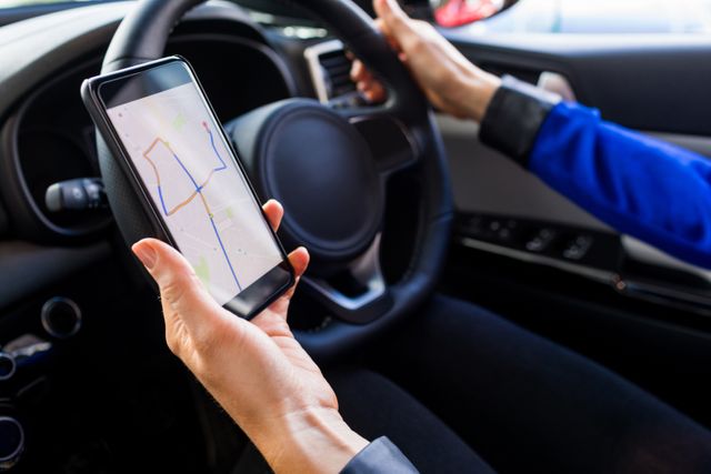 This image shows a woman using a smartphone GPS while test driving a car in a showroom. It can be used for articles or advertisements related to car sales, navigation apps, driving technology, or automotive experiences.