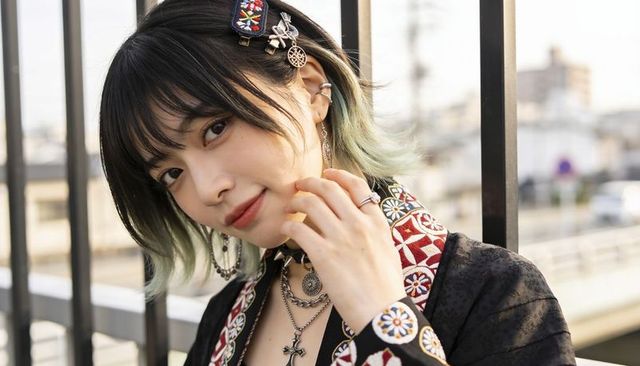 Streetstyle portrait of woman leaning on overpass wearing embroidered jacket and necklaces