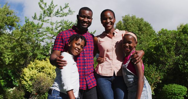 Smiling African American family posing together with lush greenery in the background. Ideal for promoting family values, outdoor activities, and mental happiness. Provides a positive image for health and lifestyle websites, corporate brochures, and community programs.