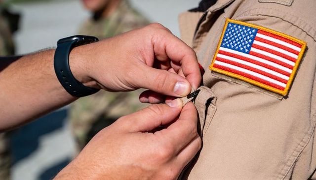 Fastening collar pin on khaki uniform with us flag patch showing teamwork and ceremony