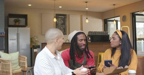 Friends Sharing Coffee and Smartphones with Barista in Cozy Cafe