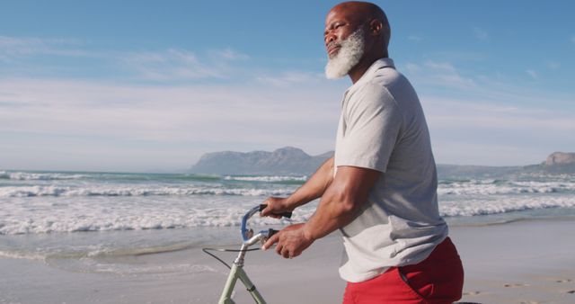 Senior african american man walking with a bicycle at the beach. healthy outdoor leisure time by the sea.