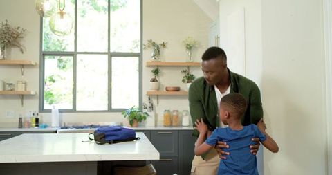 African american father hugging son in modern bright kitchen before morning school dropoff