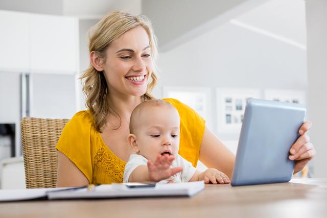 Mother looking at digital tablet with baby boy in kitchen at home