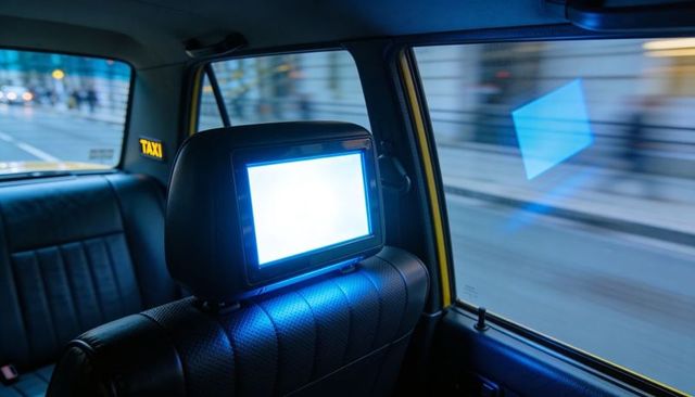 Glowing headrest monitor casting blue light over quilted leather backseat in moving taxi