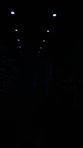 Sliding down datacenter corridor revealing blue rack LEDs and overhead lights vertical video