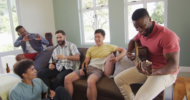 Five friends are sitting on a sofa in a cozy living room. One man plays the guitar while the others listen, hold drinks, and smile. Large windows allow natural light into the room, creating a warm and relaxed atmosphere. This scene can be used to promote social events, music, relaxation, and friendship concepts.