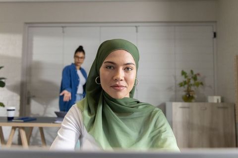 Muslim woman in green hijab leading remote team meeting in bright home office