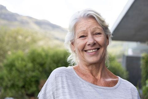 Smiling senior woman enjoying modern outdoor garden while wearing light gray knit top