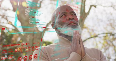 Senior man praying outdoors while interacting with augmented reality holographic interface