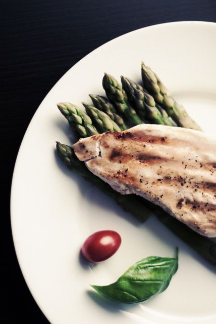 Grilled chicken breast served with asparagus, basil, and a cherry tomato on a white plate. Perfect for highlighting healthy eating, nutrition tips, and gourmet recipes. Ideal for food blogs, culinary magazines, and restaurant menus focusing on clean eating and balanced diets.
