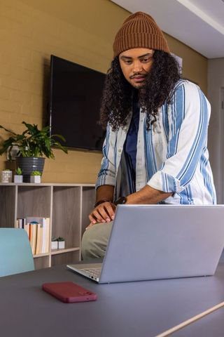 Young man leaning on table working on laptop in cozy living room with smartphone