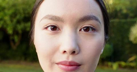 Asian Woman Posing Elegantly in Sunlit Garden Setting