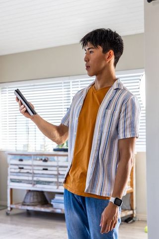 Asian man checking smartwatch while holding phone in casual modern minimalist home