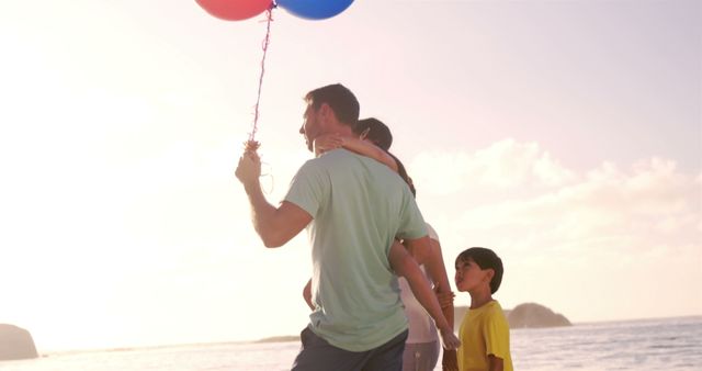 A family enjoying time together on a beach during sunset. A man holding balloons walks with family. Use for family activity concepts, summer holidays, outdoor activities, beach vacations, family moments, advertisements related to travel and leisure.