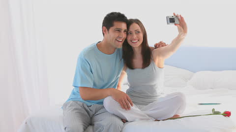 Smiling Couple Taking a Selfie in Cozy Bedroom Setting