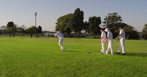 Cricket team practicing bowling drill on sunlit park field with waiting players