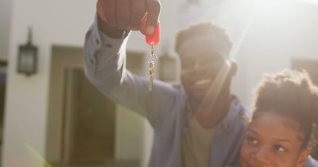Couple celebrating new home purchase by holding keys outdoors on a sunny day. Ideal for real estate advertisements, home buying promotions, mortgage offers, or lifestyle blogs about moving and new beginnings.