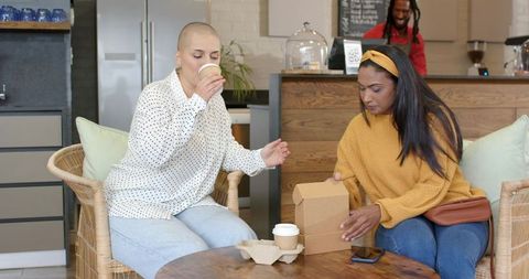 Diverse friends enjoying coffee and unpacking takeout box in cozy urban cafe