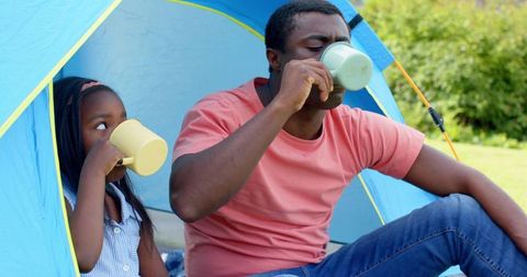 Father and Daughter Bonding While Sipping in Tent Outdoors