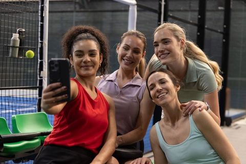 Smiling female friends taking selfie after padel match on indoor court