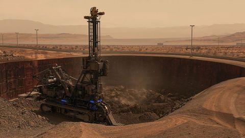 Heavy tracked drilling rig operating and excavating in desert mining pit under hazy orange light