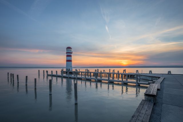 Beautiful sunset view with lighthouse and pier on calm ocean. Ideal for travel and tourism promotions, nature and marine photography, and backgrounds for websites or posters.
