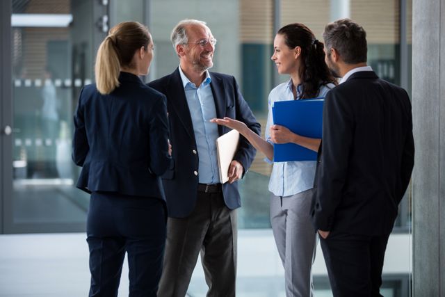 Group of businesspeople standing and engaging in a lively conversation in modern office premises. Ideal for use in corporate websites, business presentations, team-building materials, and professional networking content.