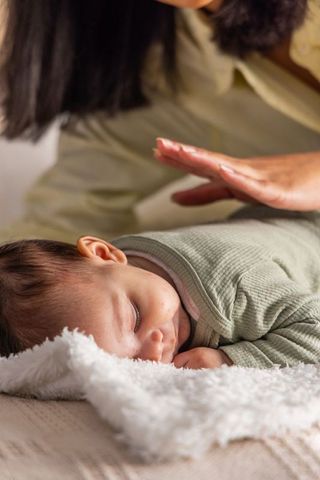 Mother leaning over sleeping baby on soft blanket showing gentle care and bonding
