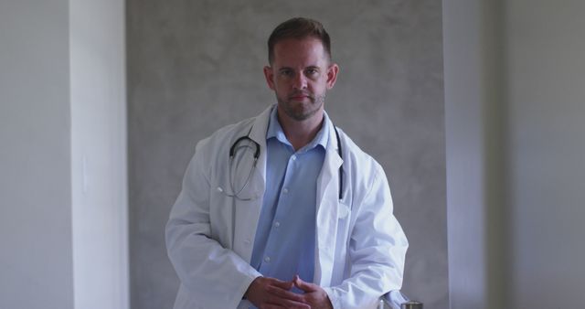 Male doctor standing indoors in a modern clinic, wearing a white coat and stethoscope, conveying confidence and professionalism. Suitable for use in healthcare advertisements, medical articles, and promotion of medical services.