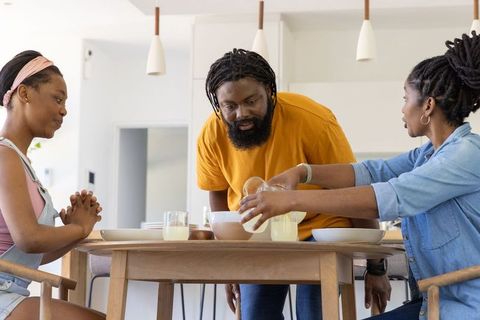 African american family sharing warm morning meal in modern kitchen, mother pouring juice