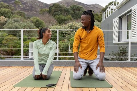 African american couple practicing outdoor yoga on wooden deck, smiling and chatting