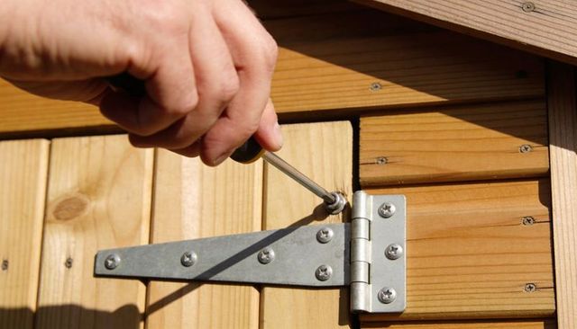Tightening t-hinge on wooden shed door with screwdriver in bright sunlight for diy repair
