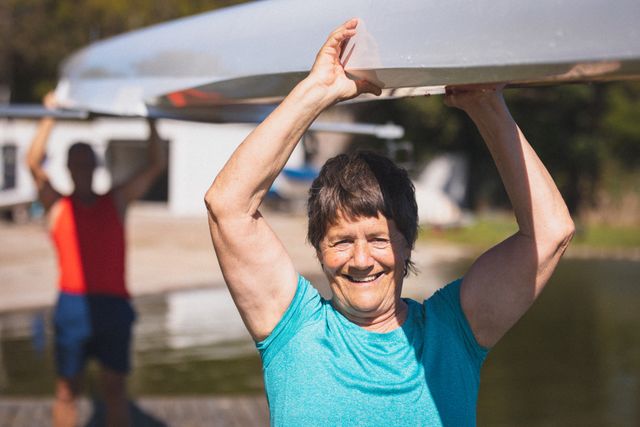 Portrait of smiling senior caucasian woman from rowing club carrying boat above her head. senior sports hobby, active retirement lifestyle.