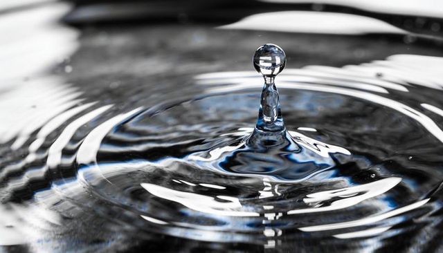 Macro water droplet rising on reflective surface with concentric ripples and glass sphere
