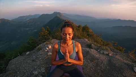 Woman meditating at mountain summit during sunrise practicing outdoor yoga and mindfulness