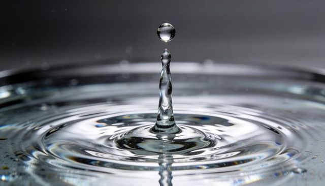 Crystal droplet suspended above slender splash column with concentric ripples on glass