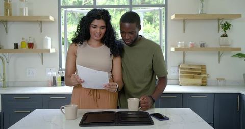 Indian and african american couple reviewing financial documents at sunlit modern kitchen