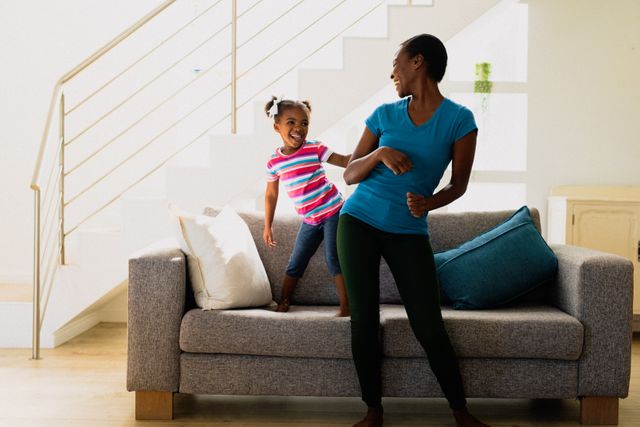 Happy african american mother and daughter dancing in living room. family, spending time together at home.