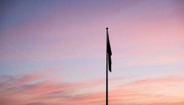 Flagpole silhouette at pastel sunrise sky, minimal vertical composition with ornate finial