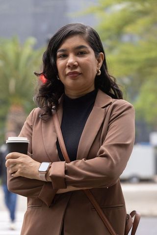 Urban professional woman standing confidently holding coffee wearing brown blazer