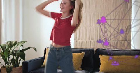 Young woman dancing in sunlit living room with navy sofa mustard cushions casual denim tee